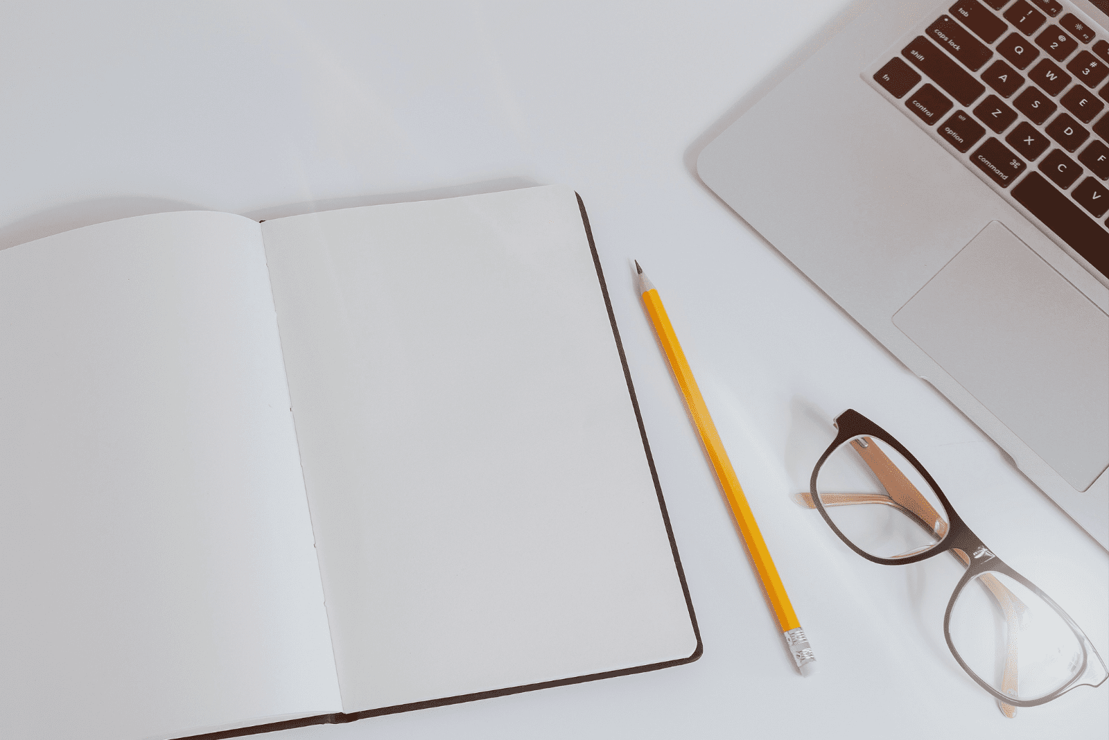 Open notebook with pencil, glasses, and laptop beside it