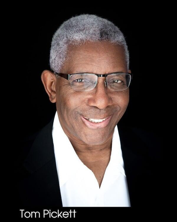 Headshot of a 50 - 70 year old Black man, glasses, black suit with white shirt, smiling.